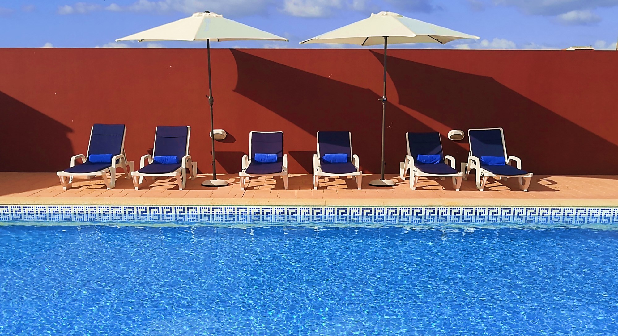 Piscina exterior da Casa do Cortiço, com guarda-sóis e parede em terracota tradicional alentejana
